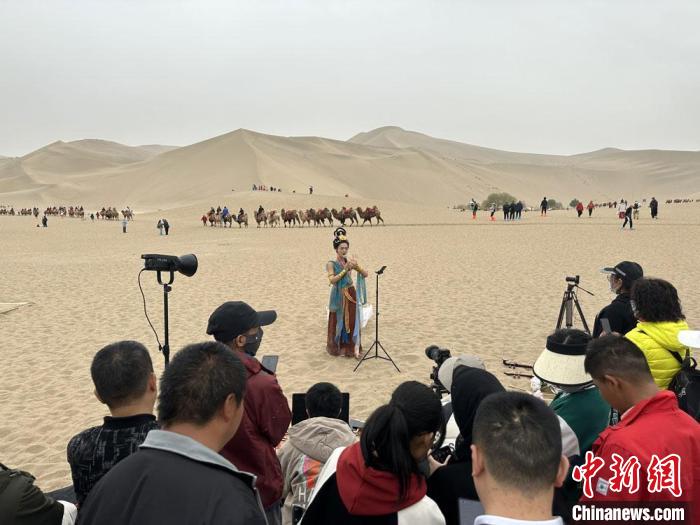 圖為2023年4月底,敦煌大漠“逐舞者”奧楠在鳴沙山月牙泉景區(qū)視頻直播,吸引游人圍觀。 馮志軍 攝 圖為2023年4月底,敦煌大漠“逐舞者”奧楠在鳴沙山月牙泉景區(qū)視頻直播,吸引游人圍觀。 馮志軍 攝